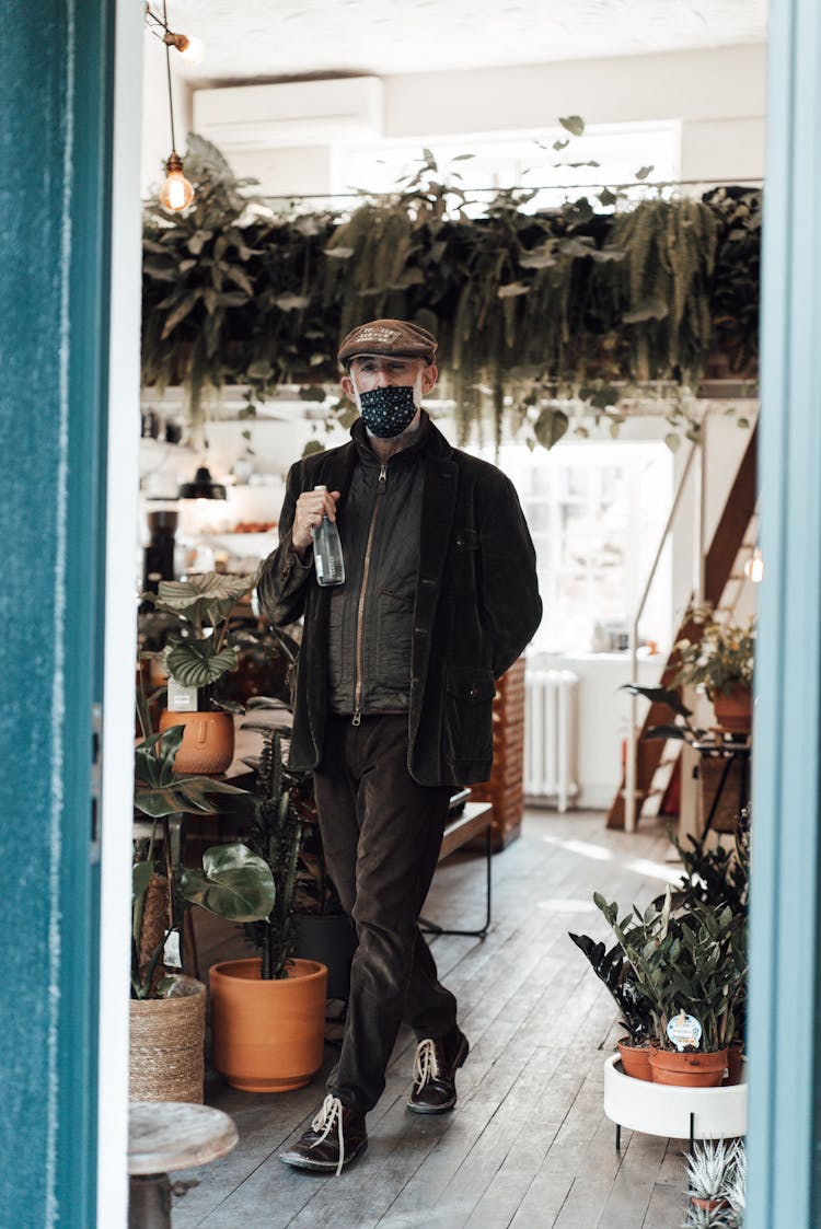 Man In Mask Standing With Bottle Of Water In Light Room