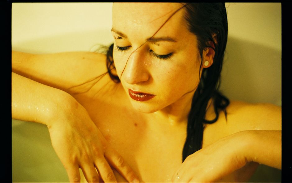 Close-up of a relaxed woman with wet hair in a bathtub, eyes closed, serene expression.