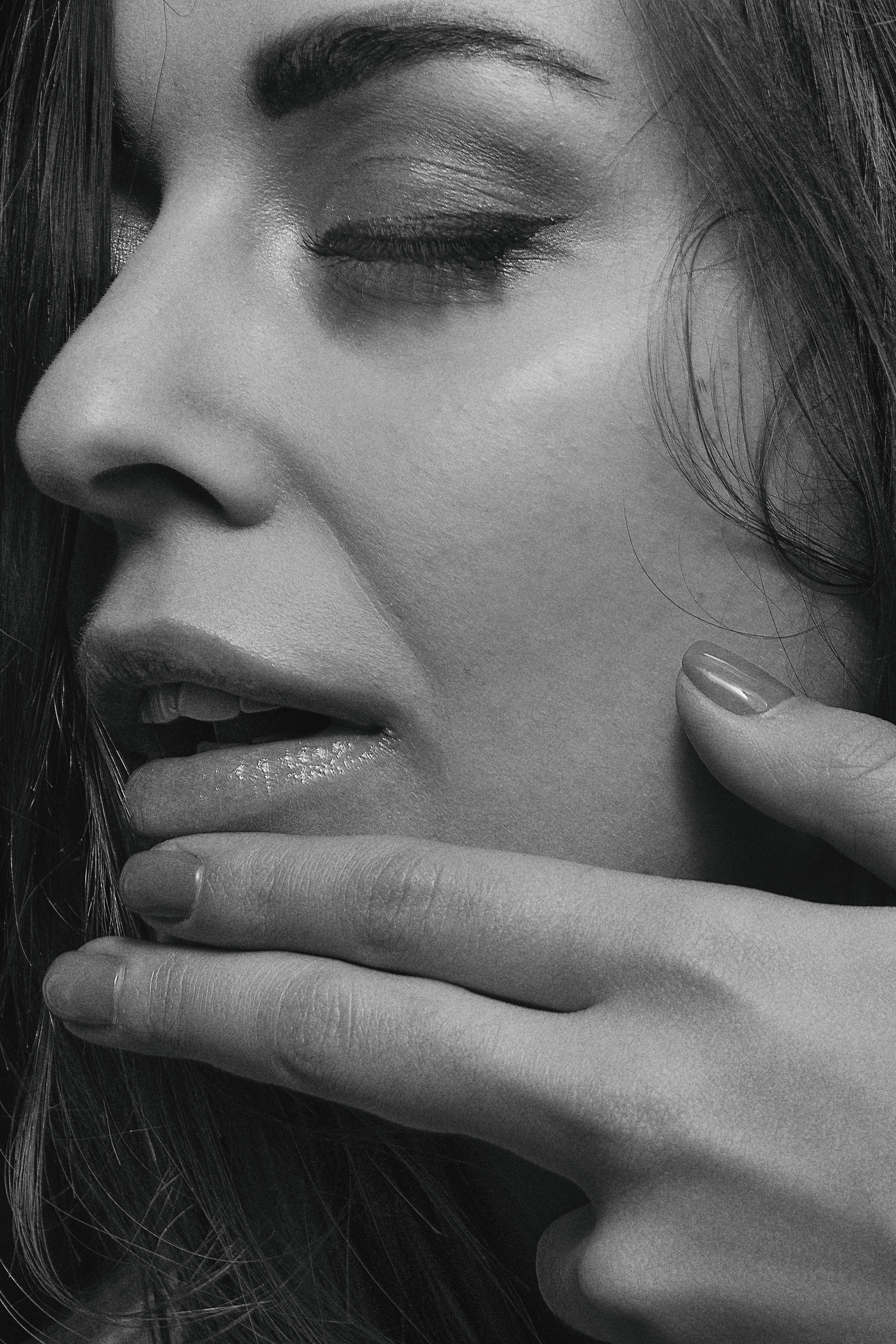 Close-up black and white portrait of a woman with hand on chin, eyes closed, capturing elegance and grace.