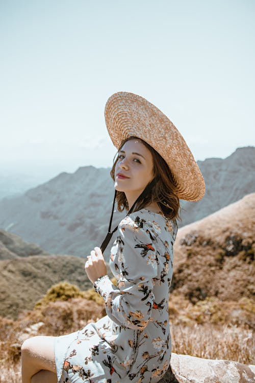 Dreamy young lady recreating on stone and admiring mountains in sunlight