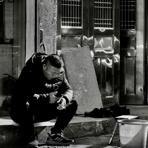 Free Black and white photo of a man smoking on a sidewalk in Wenzhou, China. Stock Photo