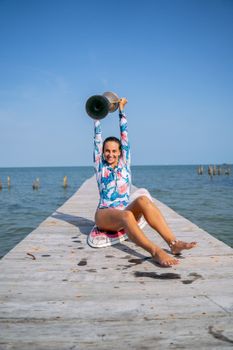 Joyful woman sitting on pier holding trophy above head, symbolizing victory and celebration near ocean.