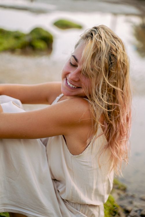 Free A joyful woman with blonde hair and closed eyes seated by the seaside, enjoying a peaceful moment. Stock Photo
