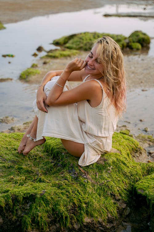 Beautiful Woman Sitting on Mossy Rock Near Water