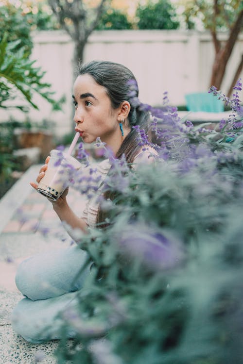 A Woman Sipping Milk Tea while Sitting Near Lavender Flowers