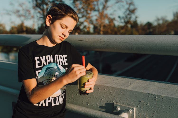 A Child With A Black Shirt Holding A Milk Tea