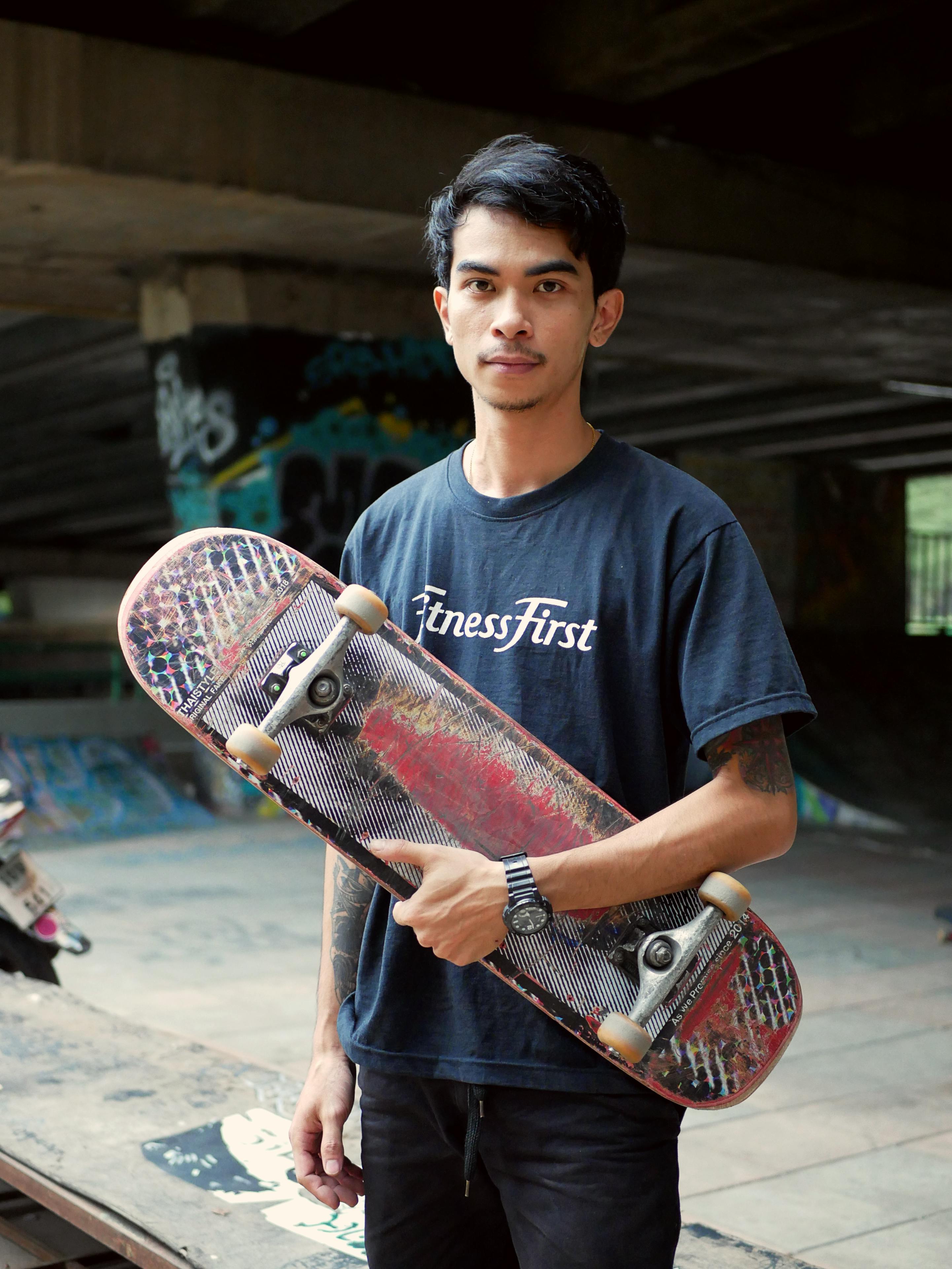 Portrait of a young man holding skateboard in a graffiti-covered skatepark.