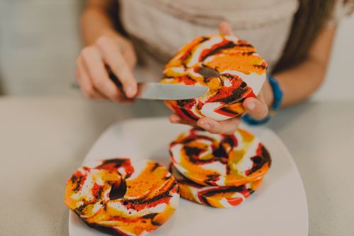 Free Close-up of colorful swirled bagels being spread with cream cheese, showcasing food artistry. Stock Photo