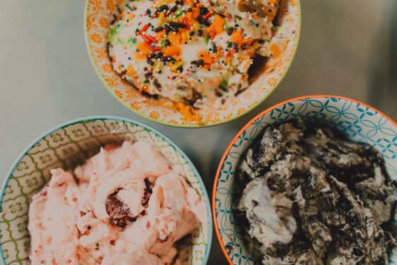 Three patterned bowls of ice cream with sprinkles, pink strawberry swirl and chocolate cookie chunks