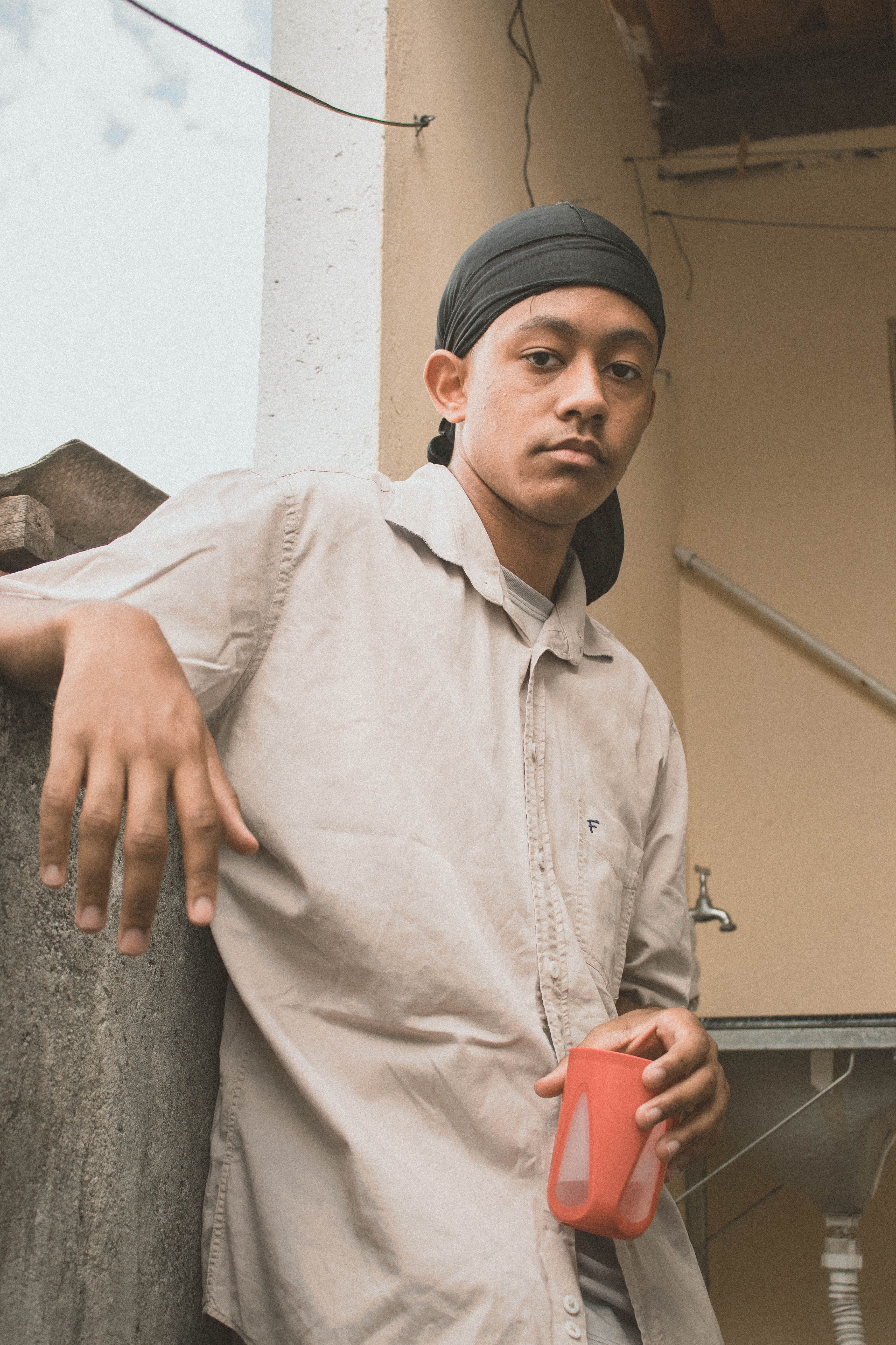 Portrait of a man holding a red cup, wearing a headscarf, casual setting.
