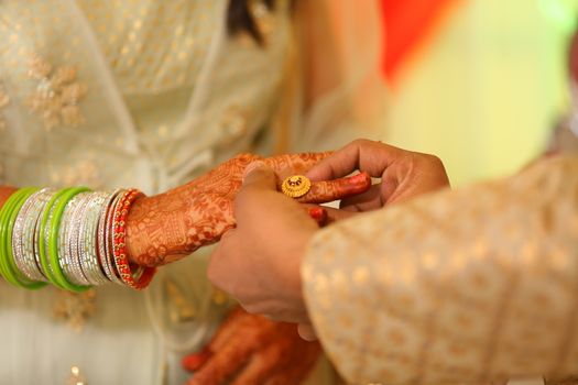 Close-up of a couple exchanging rings with intricate mehendi and colorful bangles, highlighting a traditional Indian wedding.
