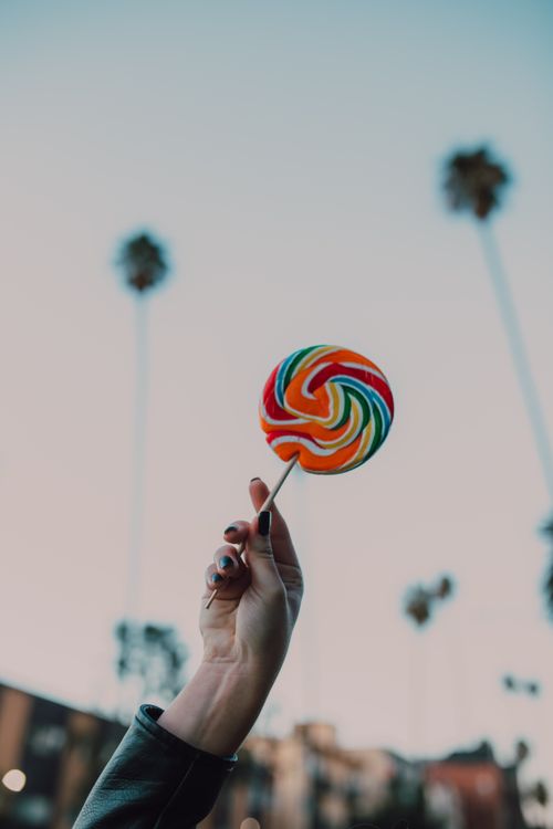 Free Colorful lollipop held up towards a clear sky with palm trees in background. Stock Photo