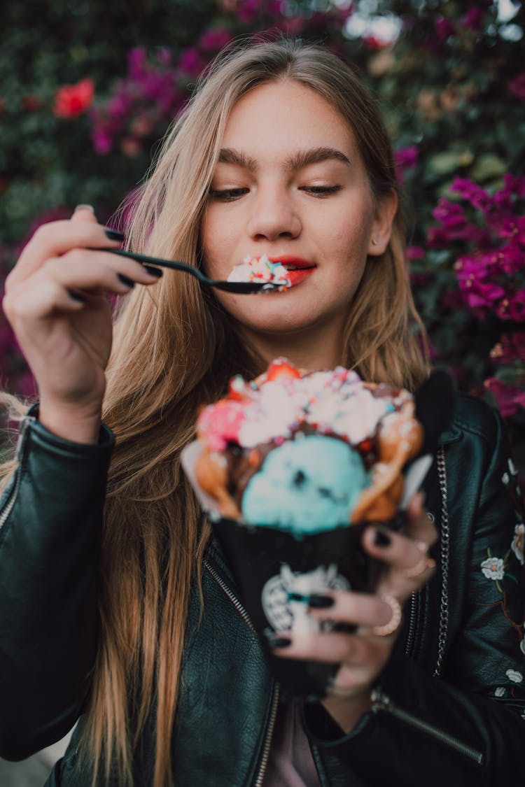 A Woman In A Black Leather Jacket Eating An Ice Cream