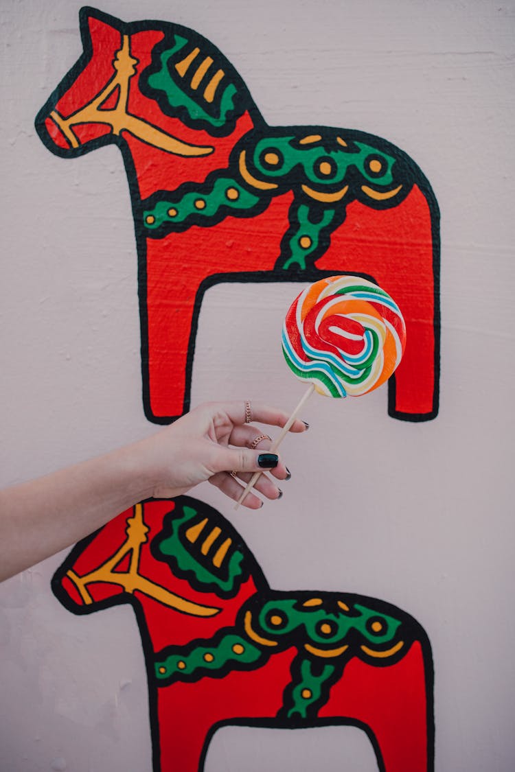 Hand Holding Lolipop In Front Of Art Of Horses