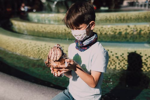 茶色のチョコレートアイスクリームを保持している白いtシャツの少年