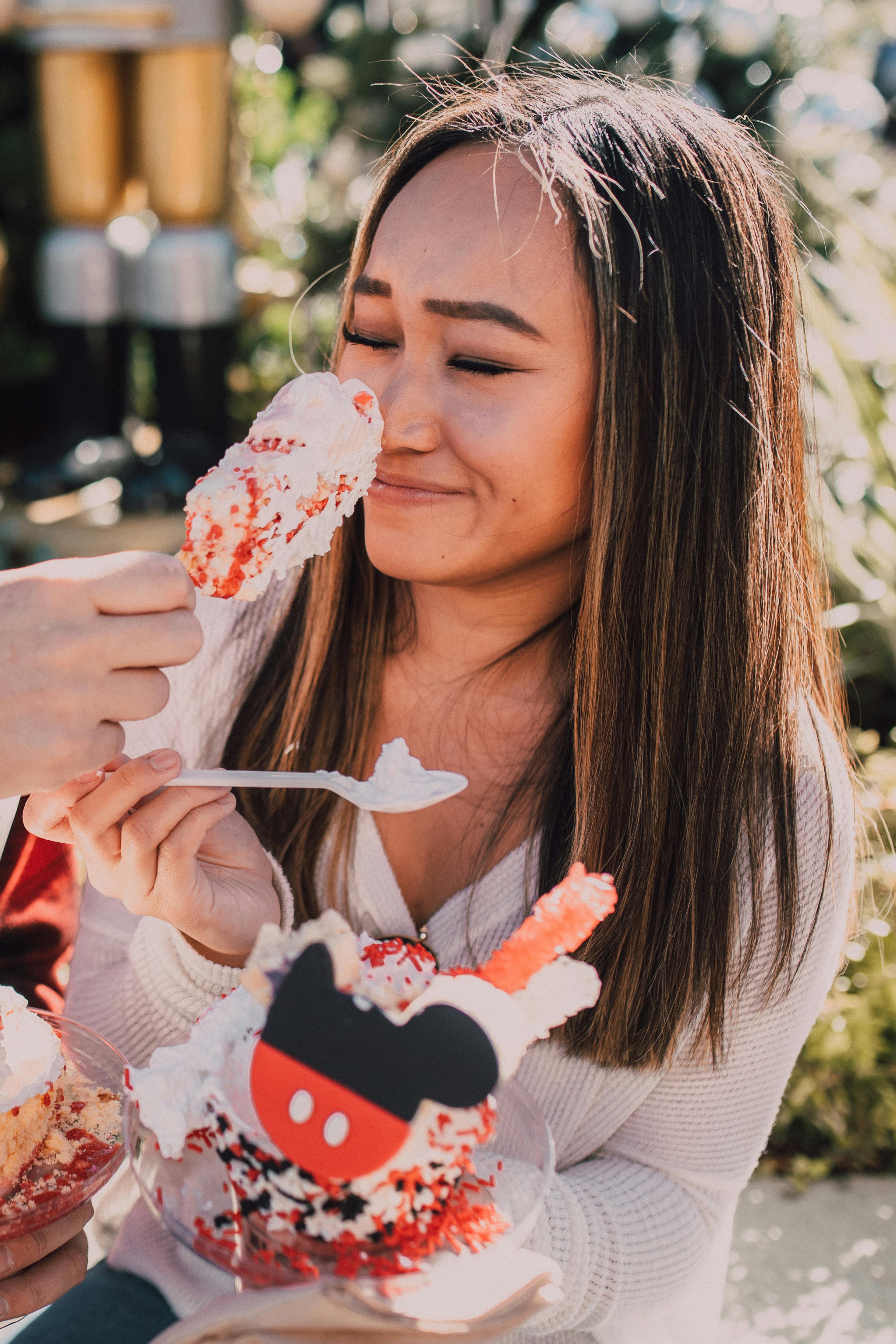 A young woman playfully enjoying a colorful dessert outdoors, surrounded by sunlight and joy.