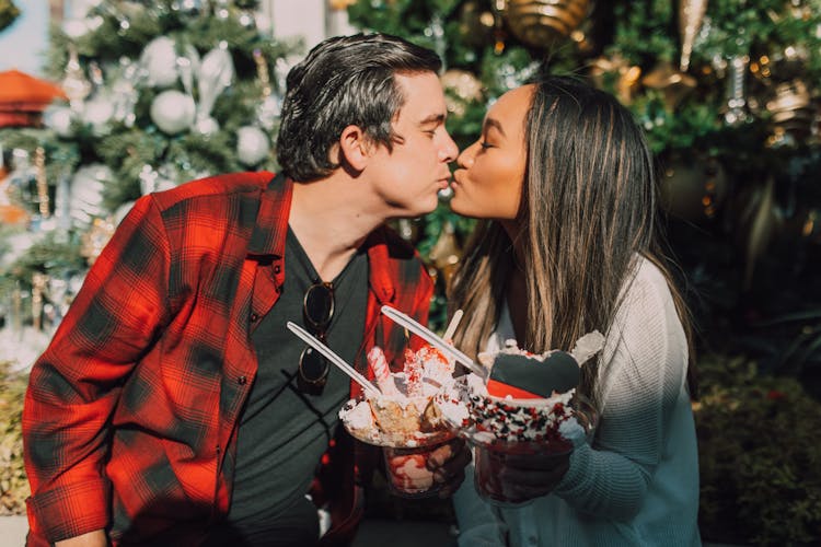 A Couple Kissing While Holding Ice Cream