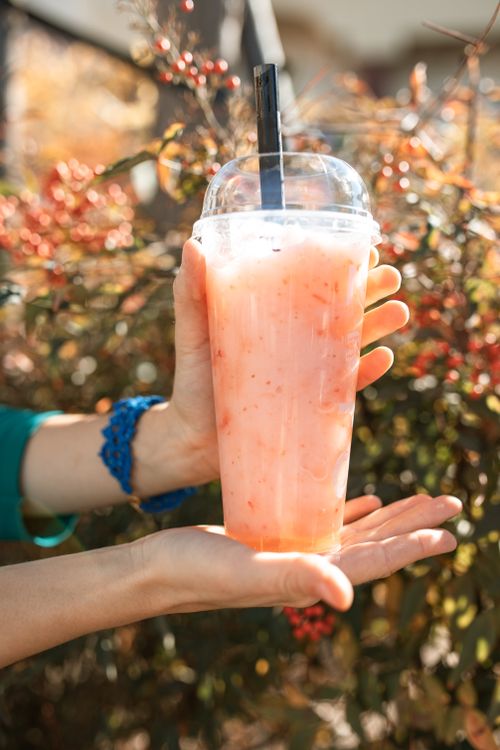 Free Close-up of a refreshing iced strawberry drink held outdoors against a leafy background. Stock Photo