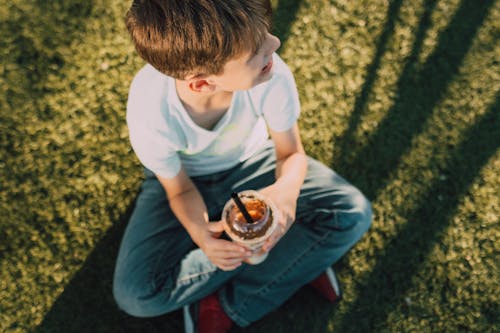 Boy in White Crew Neck T-shirt and Blue Denim Jeans Sitting on Green Grass Field