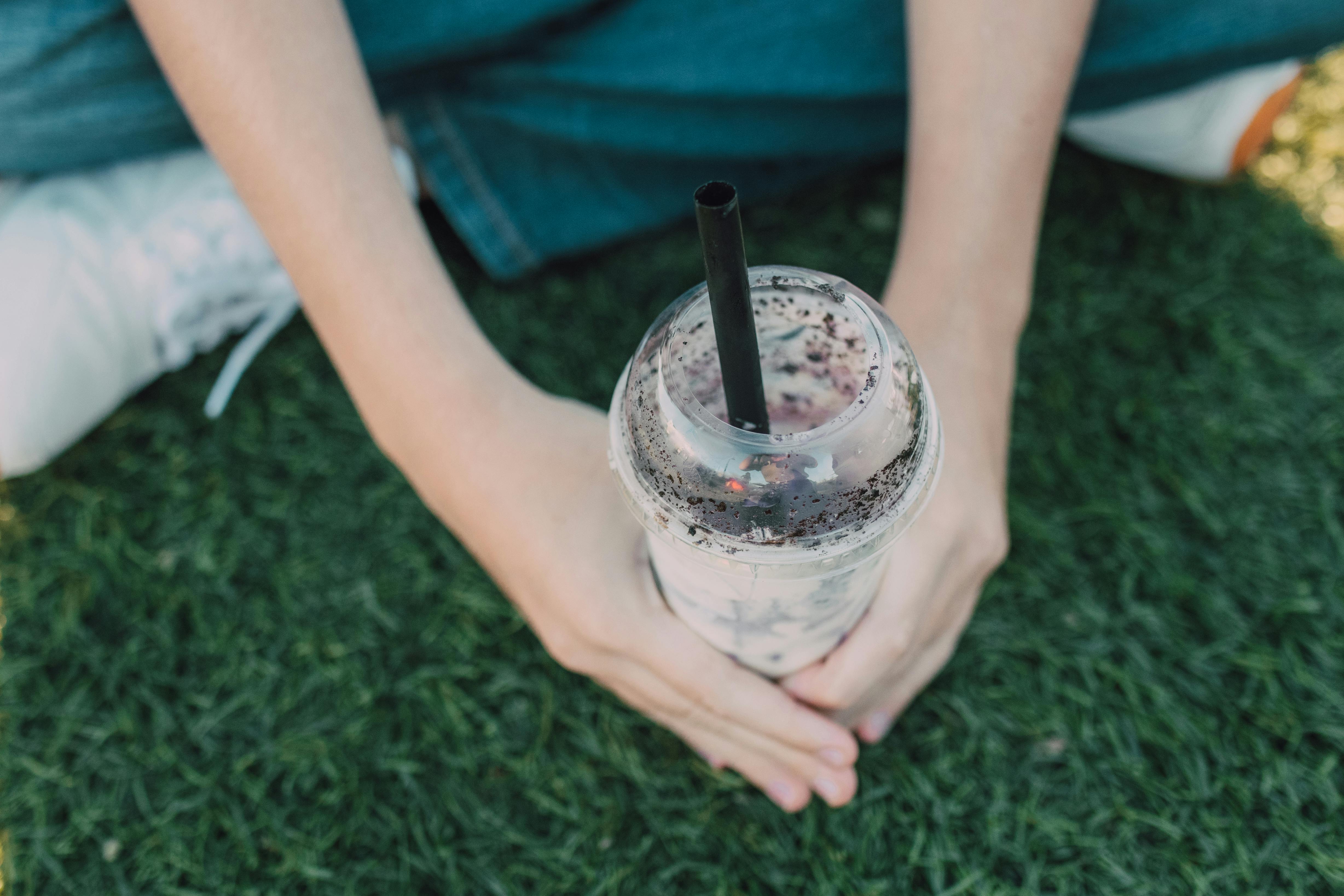 person holding clear glass cup with black straw