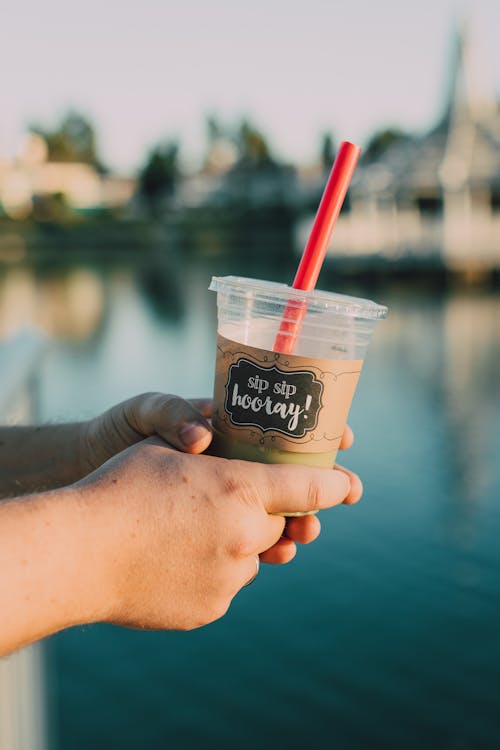 Person Holding a Plastic Cup With Red Straw 