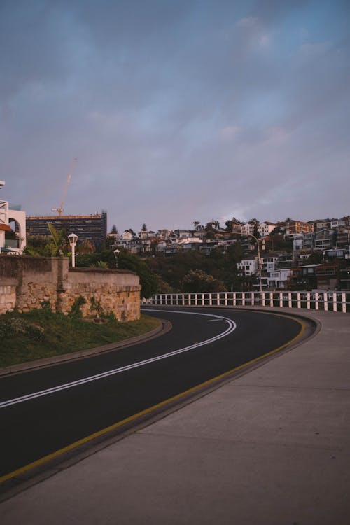 Curvy road in mountainous town under cloudy sky at sunset