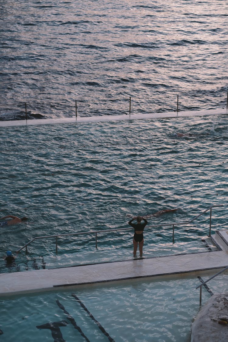 Anonymous People Swimming In Pool Near Ocean At Sunset