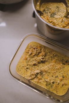 From above of delicious homemade soup with chicken and herbs in metal saucepan and glass container placed on white table