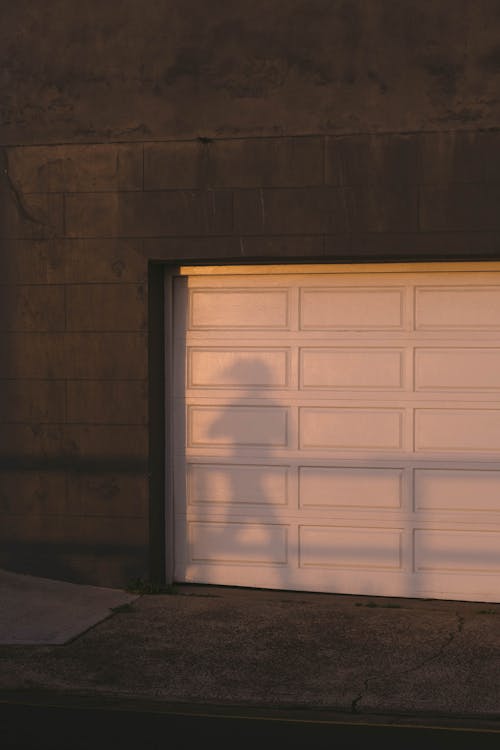 Shadow of unrecognizable person running on city street near stone building with white gates at sunset