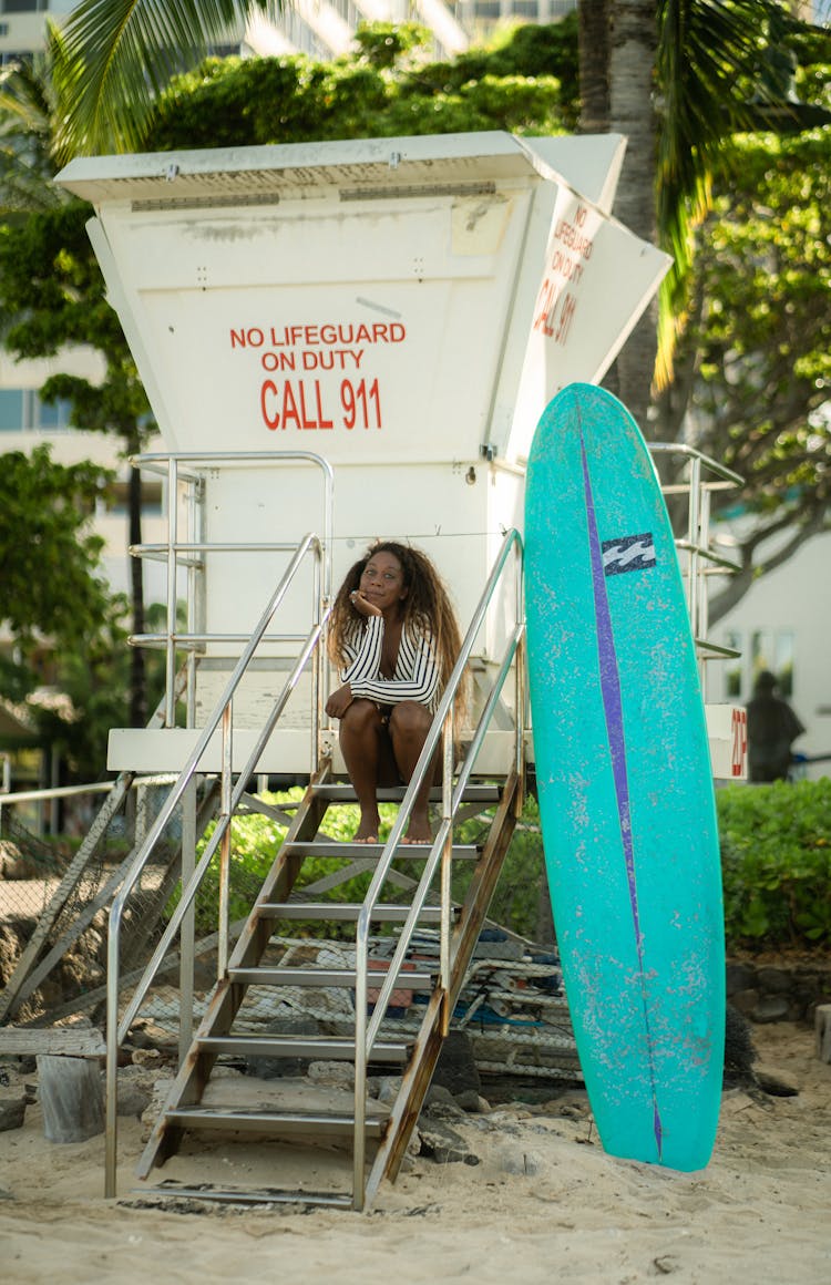 Positive Black Woman Sitting On Lifeguard House Staircase On Beach