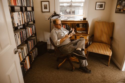 Free An adult man in a home library reading a smartphone, surrounded by books. Stock Photo
