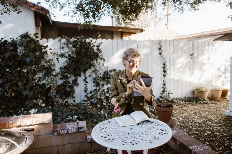 Senior woman enjoying tablet in outdoor garden setting, smiling and relaxed.