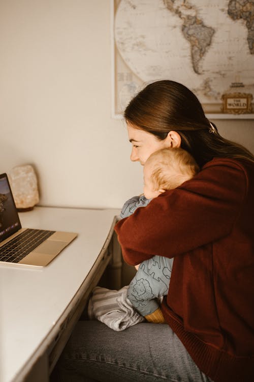 Free Mother Carrying her Baby while Looking at Laptop Stock Photo