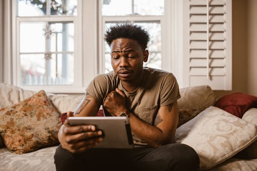 Emotional Man Sitting on Couch Watching a Video on Tablet