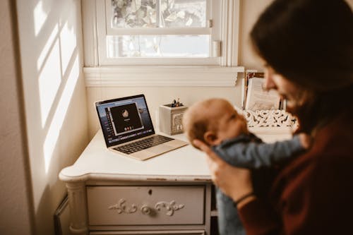 Woman Holding Her Baby while Having a Video Call Using a Laptop