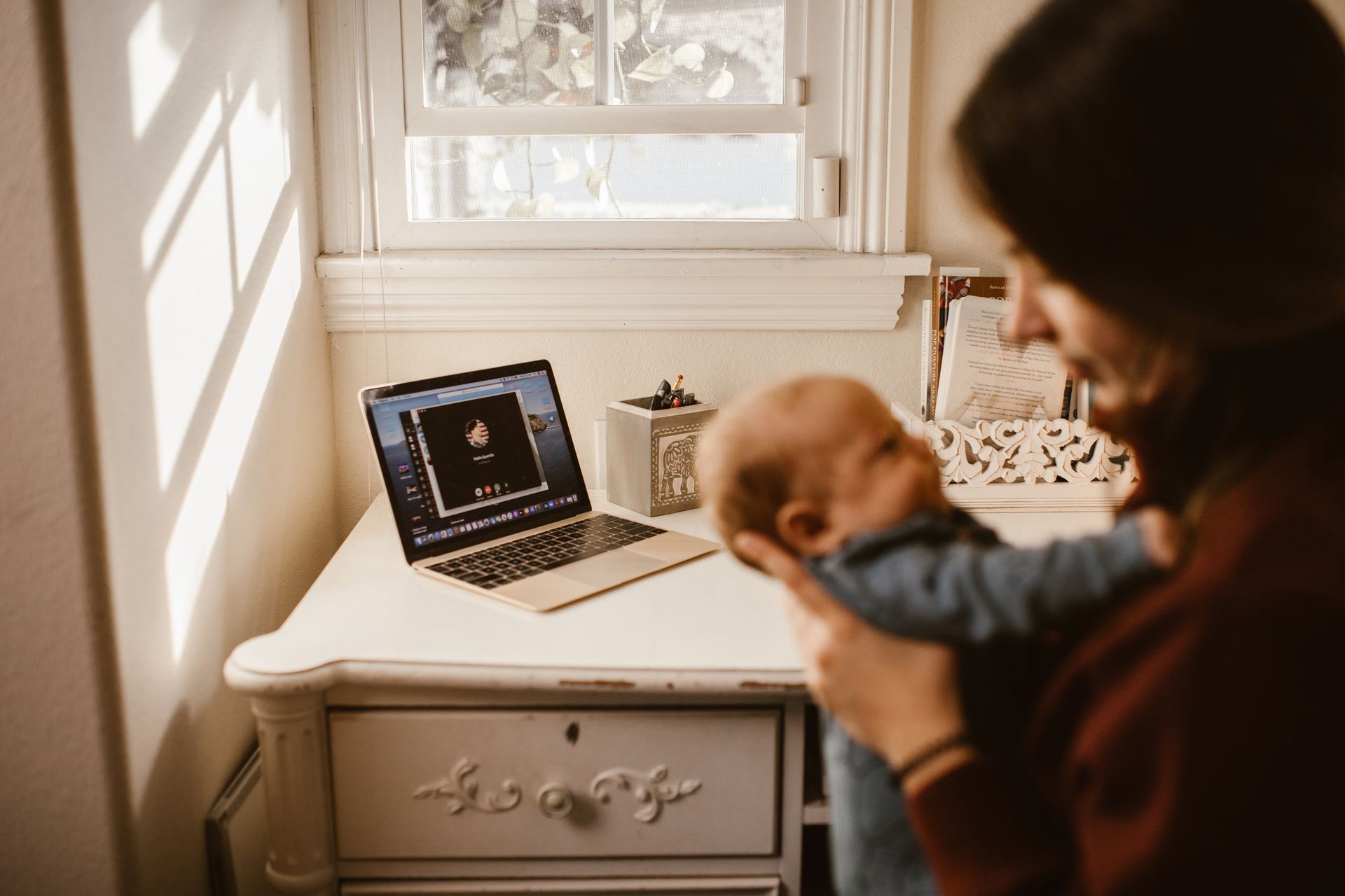 A mother holding her baby while on a video call indoors, showcasing modern connectivity and family love.