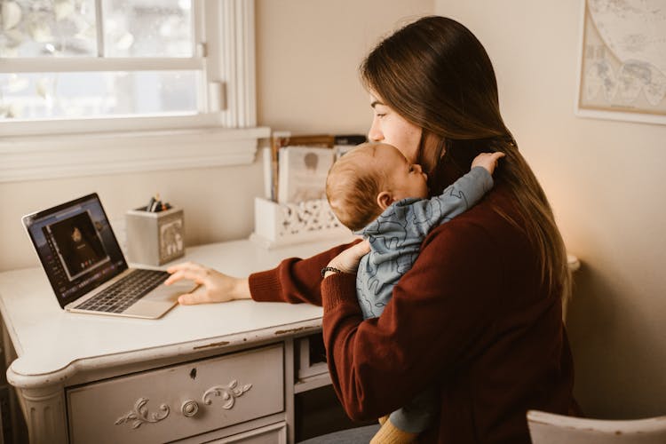 Mother Carrying Her Baby While Calling Her Husband On Laptop