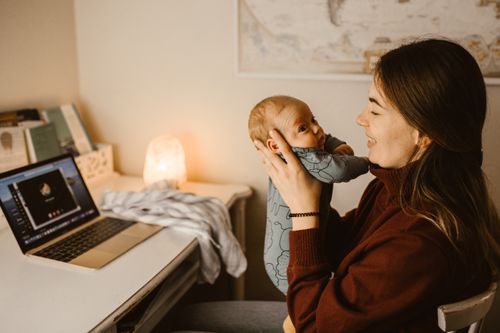 Free Mother holding baby while video calling from home office. Cozy and heartwarming indoor scene. Stock Photo
