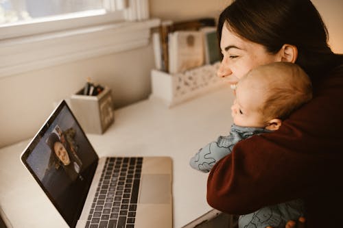 Woman Holding Her Baby while Having a Video Call Using a Laptop