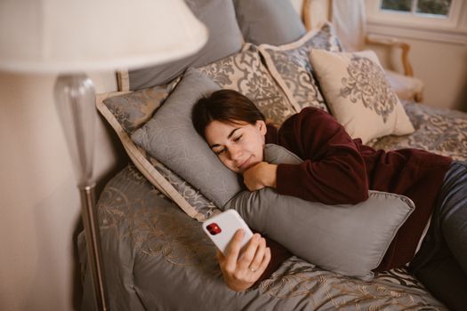Woman in a cozy bedroom using a smartphone for video call, embracing connection.