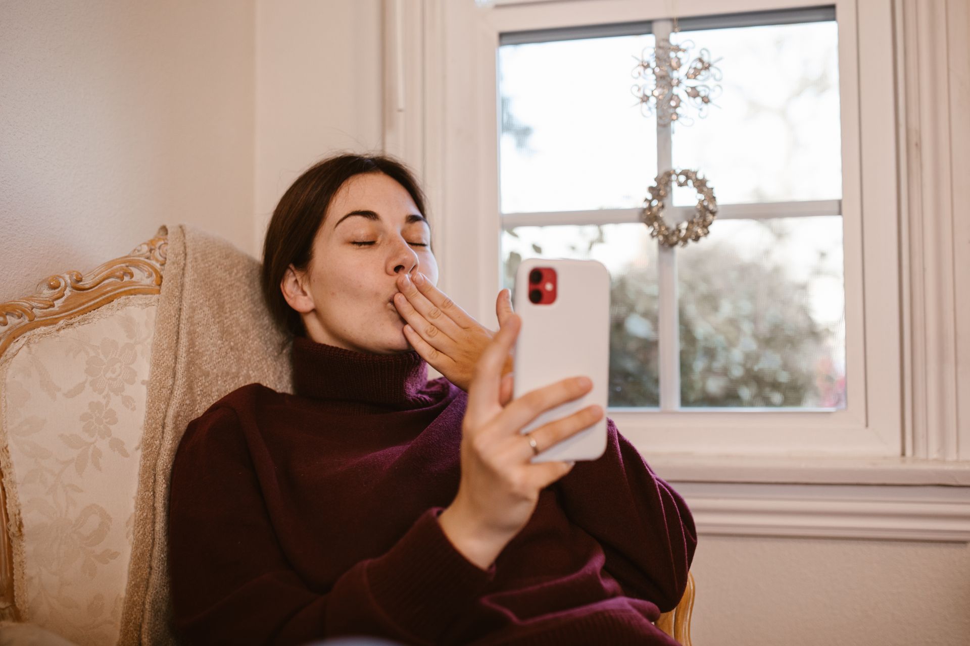 A woman blowing a kiss during a video call on her smartphone at home, symbolizing connection and affection.