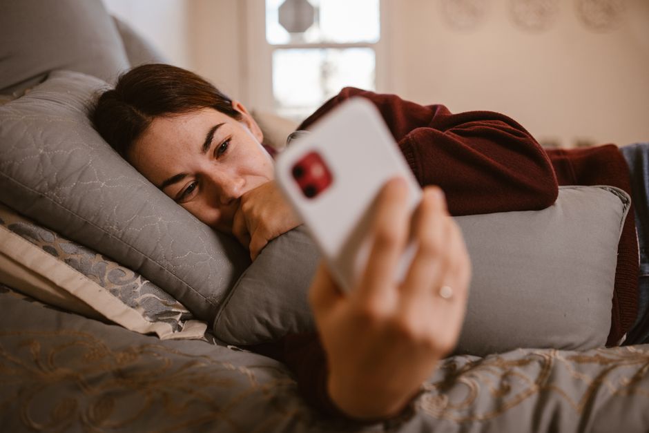 Does Mouth Taping Actually Help with Snoring and Sleep Apnea? A woman lies comfortably on a bed, using her smartphone in a cozy indoor setting.