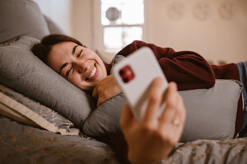 Free A Woman Using Her Smartphone while Lying Down in Bed Stock Photo