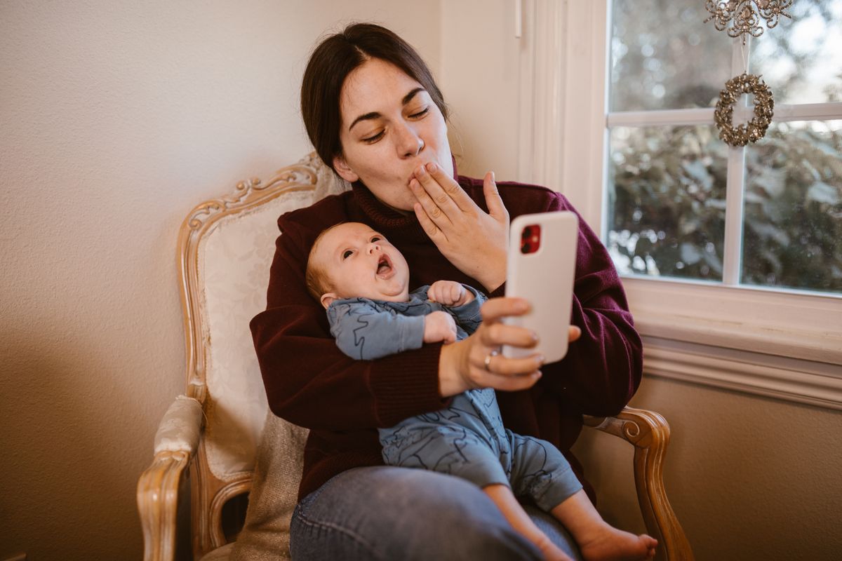 Mother holding her baby while using a smartphone at home
