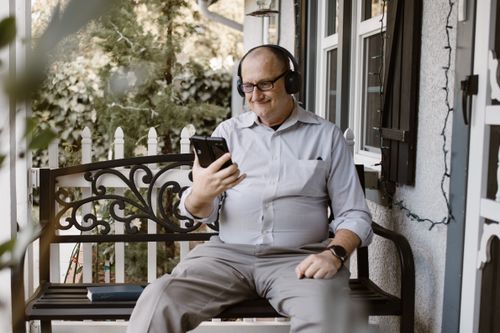 Free Senior man on porch engaging in a video call using a smartphone, relaxed setting. Stock Photo