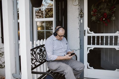 Free Elderly man enjoying music on porch, wearing headphones and checking phone. Stock Photo