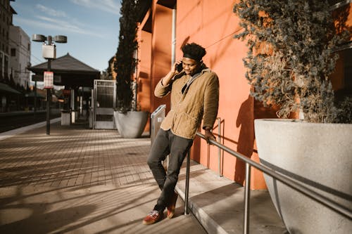 Kostnadsfri bild av afroamerikansk man, använder mobiltelefon, beige kappa