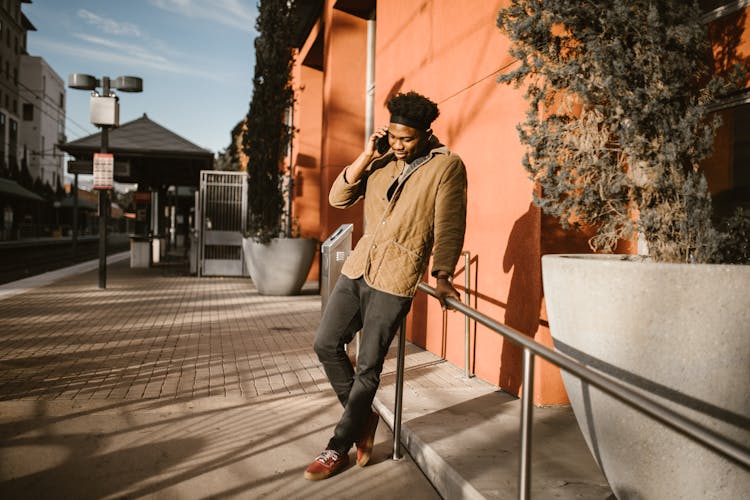 Man In Beige Coat Using A Cellphone And Leaning On A Steel Handrail On Sidewalk