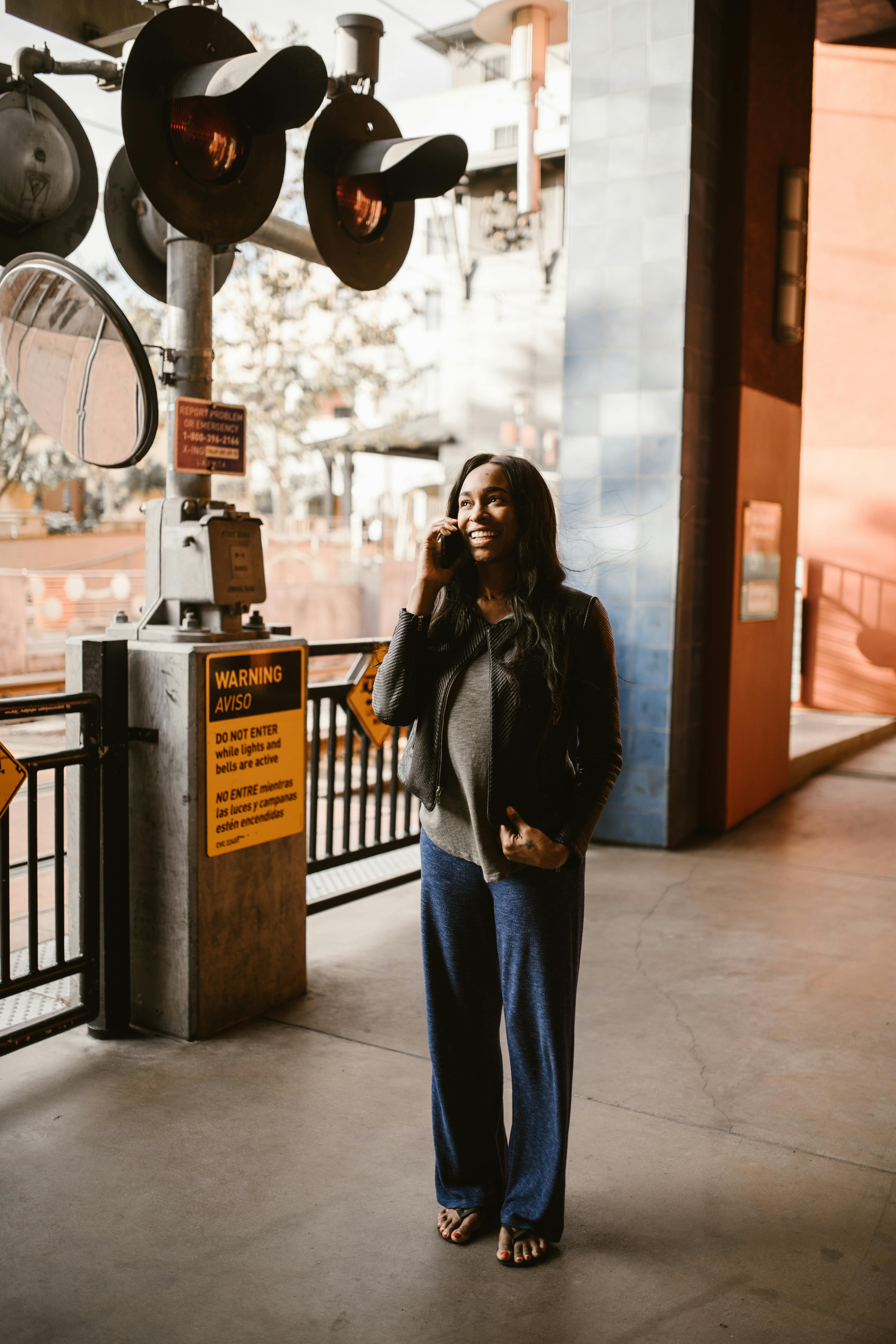 woman in black leather jacket and blue denim jeans standing near black metal fence