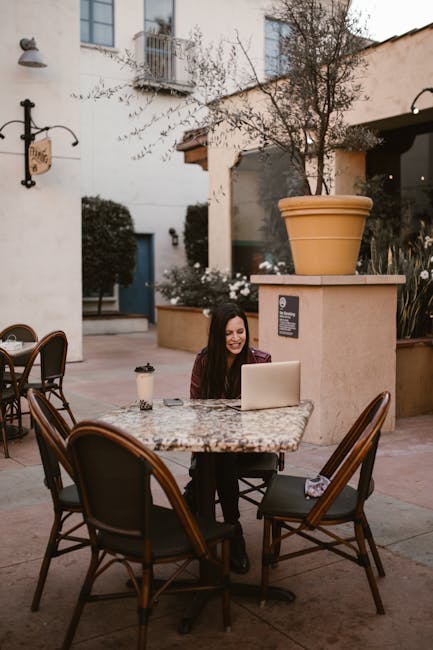 A woman enjoys remote work on a laptop in an outdoor cafe setting.